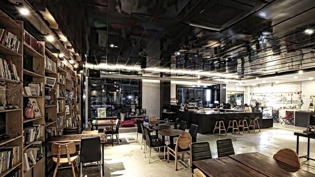 A modern library with bookshelves, tables, and chairs, and a coffee bar in the center. - Jeonju Hostel (Jeonju)