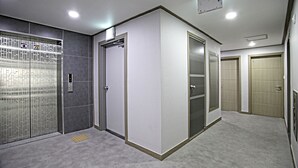 A modern elevator area with a glass elevator door, a control panel, and a plain wall with a door to another room. - Jeonju Hostel (Jeonju)