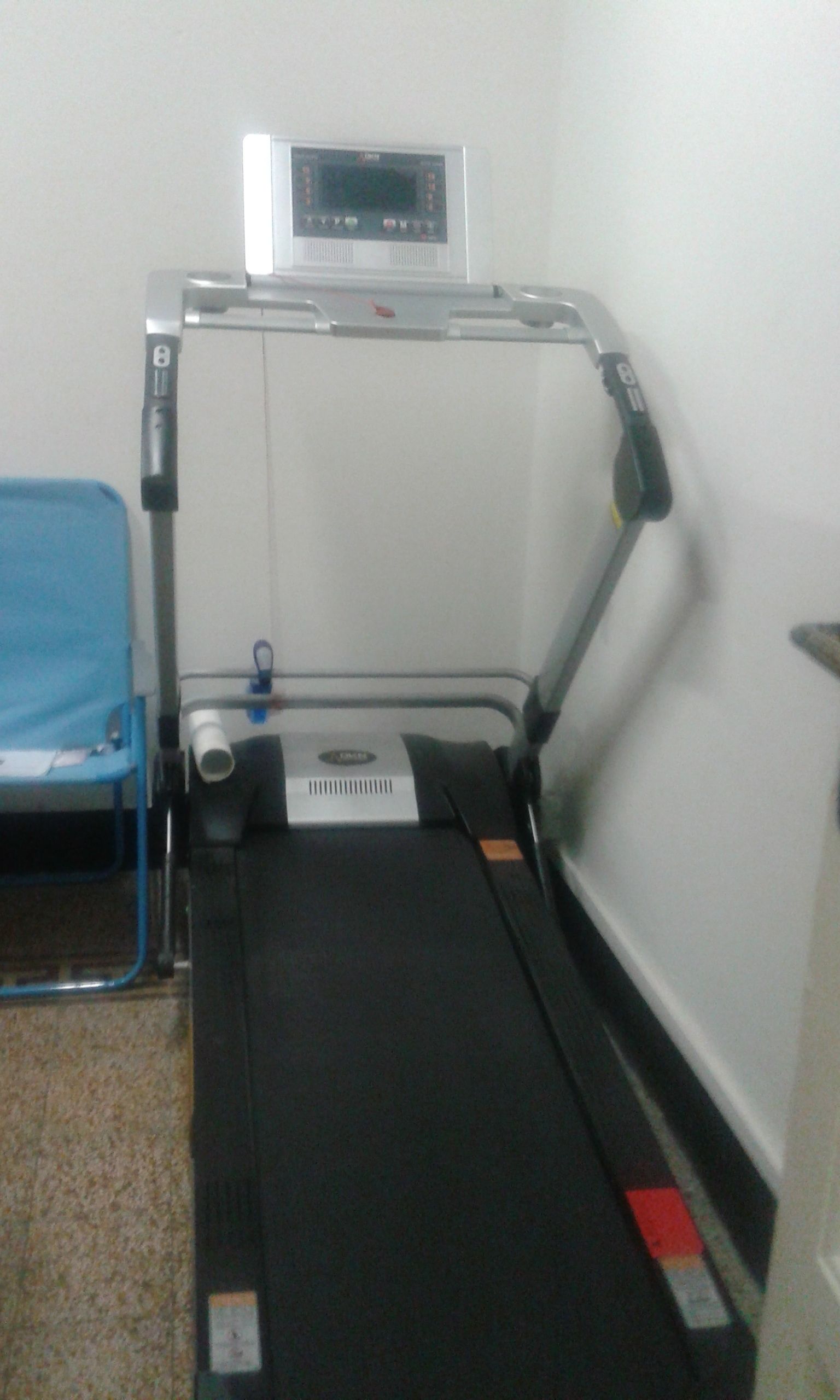 A treadmill in a room with a blue chair and a white wall.