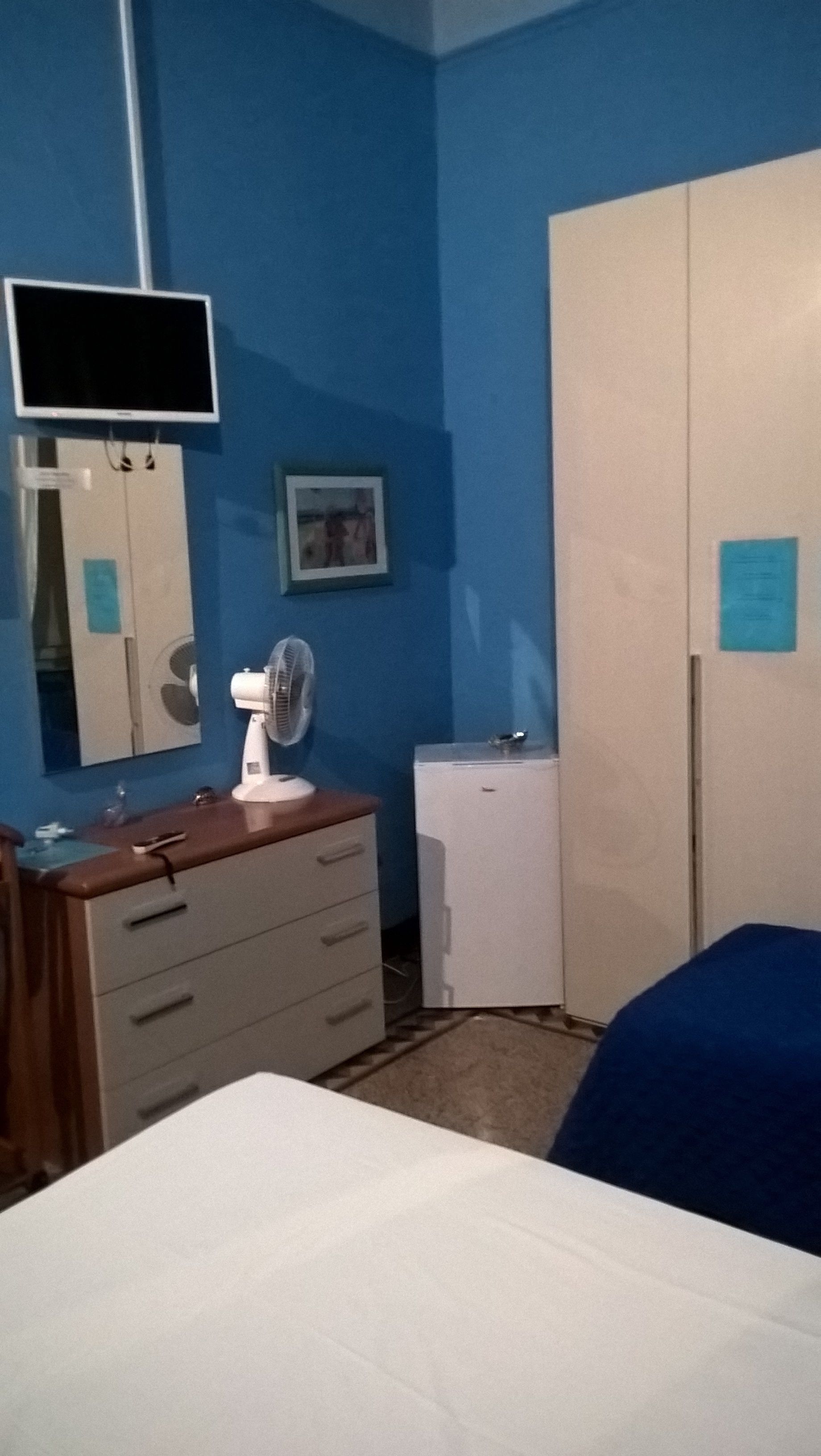 A bedroom with a bed, dresser, mirror, fan, and wardrobe.