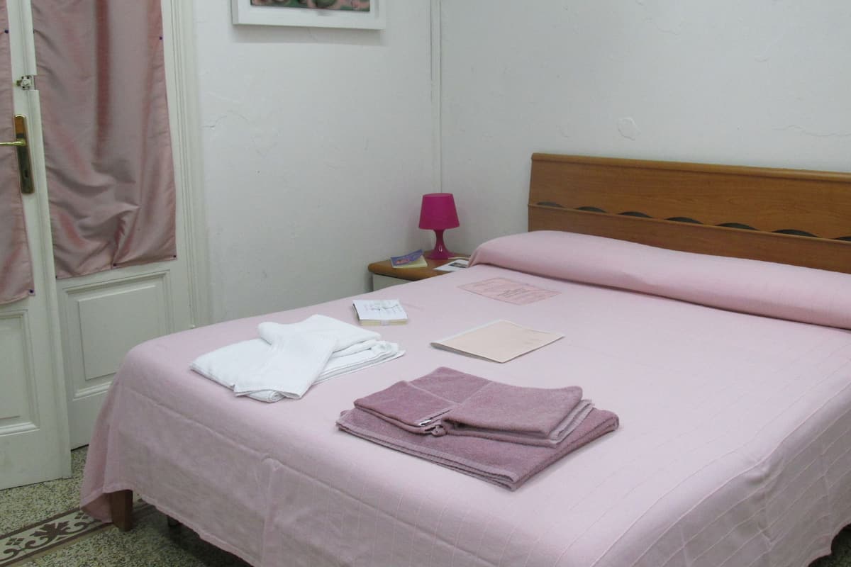 A neatly made bed with pink bedding, a wooden headboard, and a pink lamp on a bedside table.