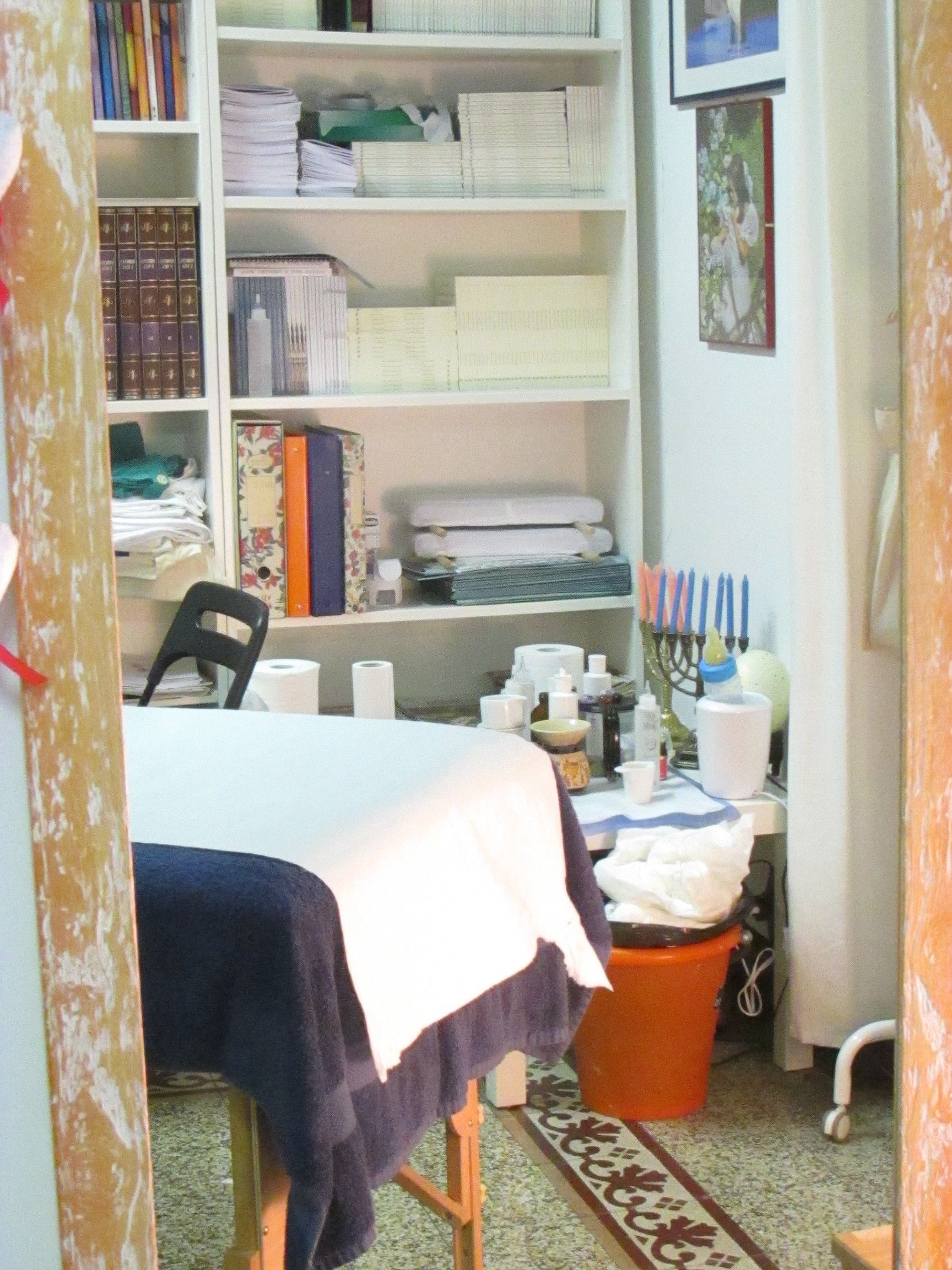 A small room with a bed, a chair, a desk with a computer, and a bookshelf filled with books and binders.