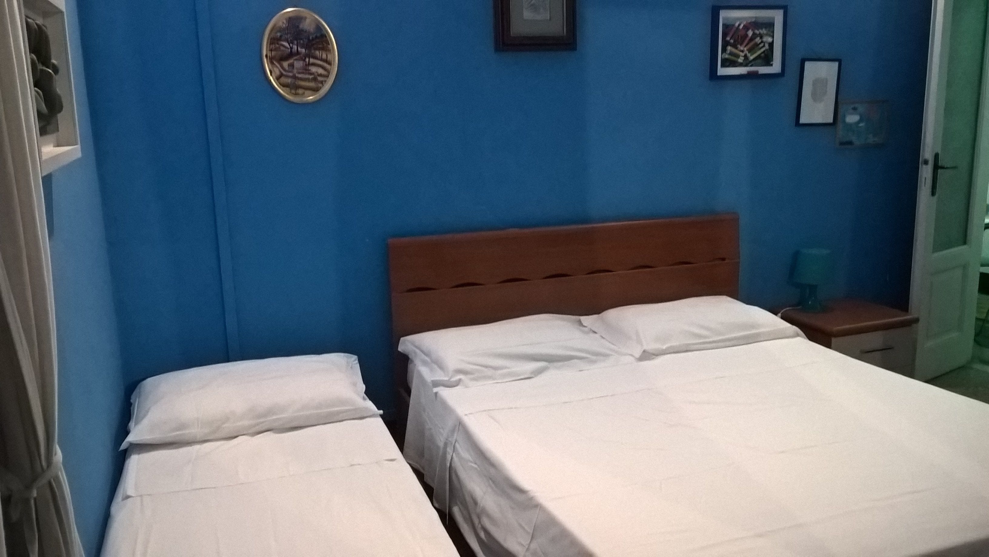 Una camera da letto con due letti, una testiera in legno, un muro blu e un piccolo comodino con una lampada.