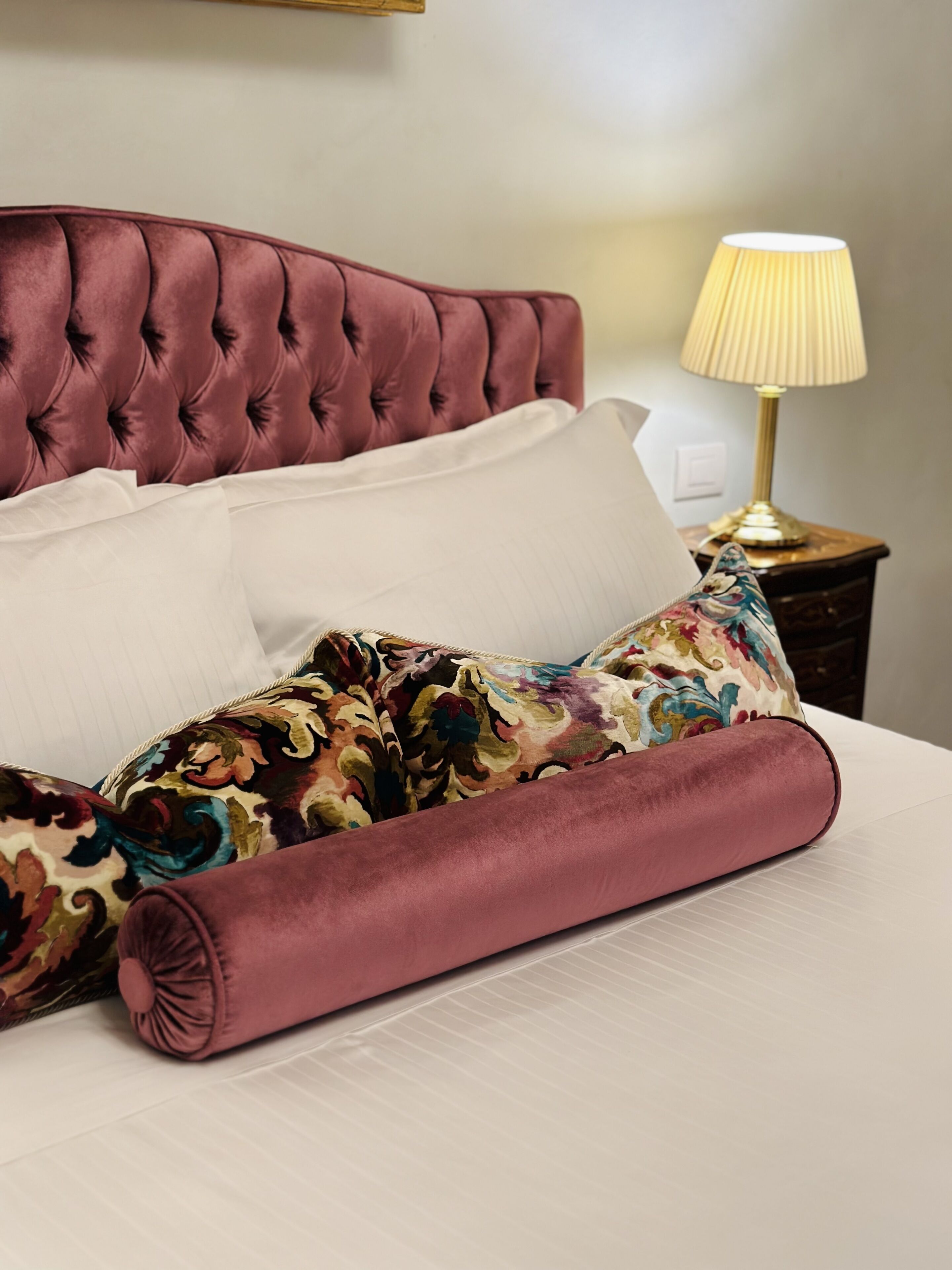 A neatly made bed with a tufted headboard, white pillows, and a floral-patterned blanket.