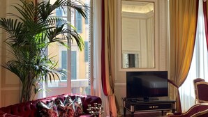 Uma sala de estar luxuosa com um sofá vermelho, uma mesa de centro de vidro, uma planta em vaso grande, um lustre e uma televisão.
