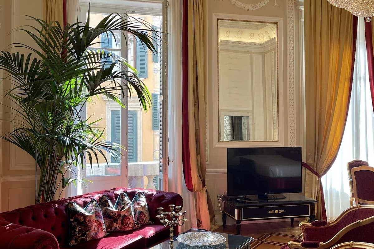 A luxurious living room with a red sofa, a glass coffee table, a large potted plant, a chandelier, and a television.