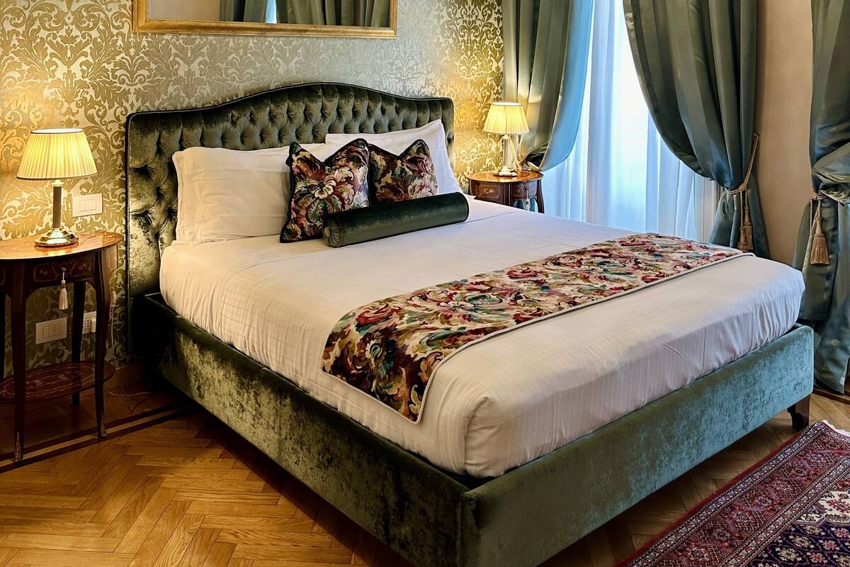 A luxurious bedroom with a tufted headboard, a large mirror, and a chandelier.