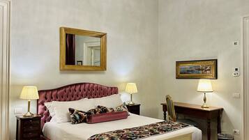 A bedroom with a large bed, two bedside tables with lamps, a mirror, a picture frame, and a chandelier.
