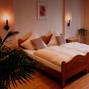 Una cama bien hecha con estructura de madera, una mesita de noche con lámpara y un aplique de pared.
