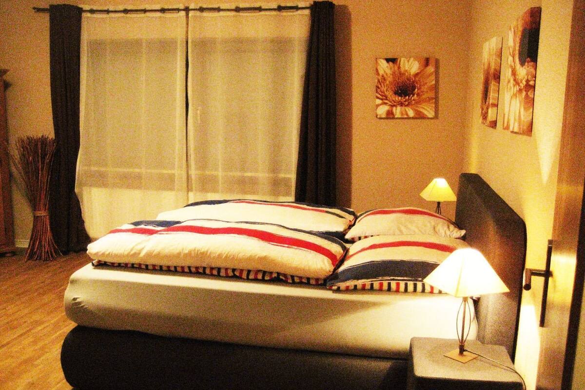 A neatly made bed with a striped pillowcase, a bedside lamp, and a wall with two framed pictures.