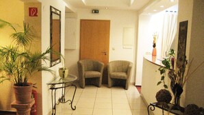 A hotel lobby with a tiled floor, two armchairs, a small table, a potted plant, and a mirror on the wall. - Hotel zum Schnackel (Wiesbaden)