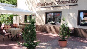 A patio area with tables and chairs, potted plants, and a building with a sign reading "Hotel zum Schnackel". - Hotel zum Schnackel (Wiesbaden)