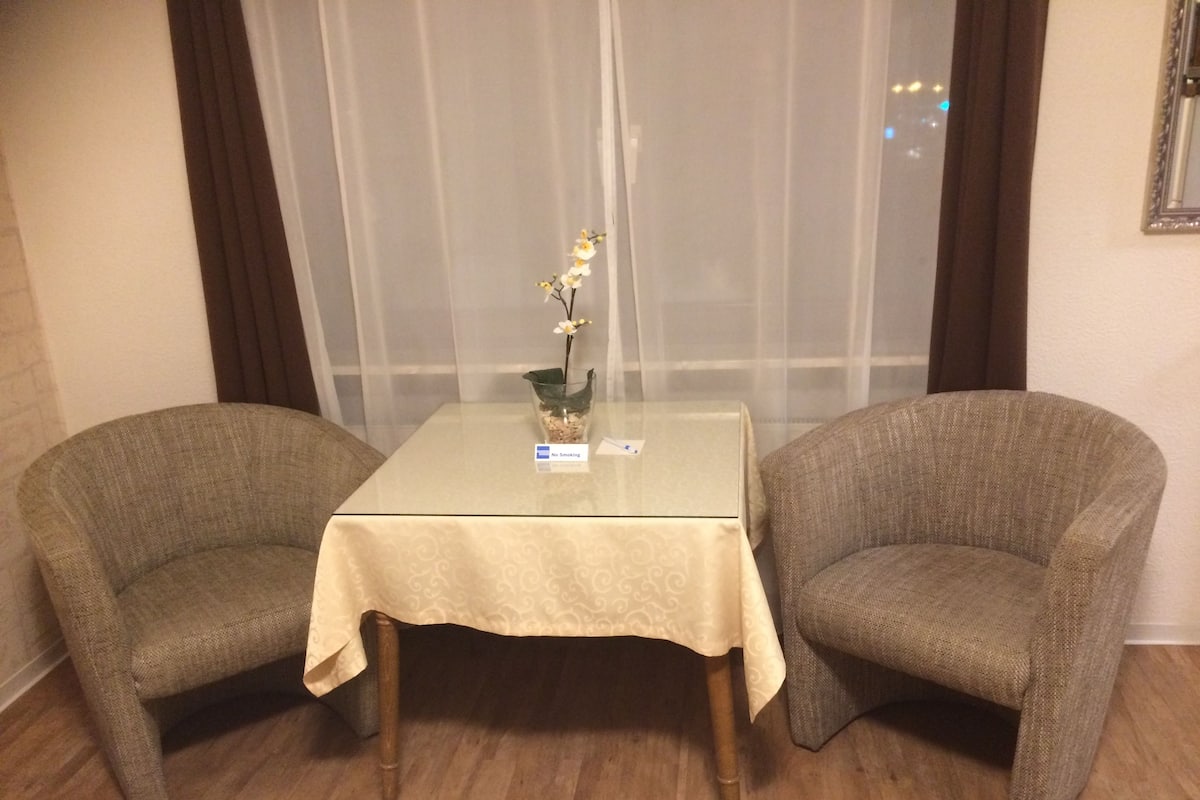 A room with two armchairs and a small table, a 'No Smoking' sign, and a window with curtains.