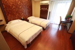 Una habitación de hotel con dos camas, piso de madera, un escritorio con silla y un armario.