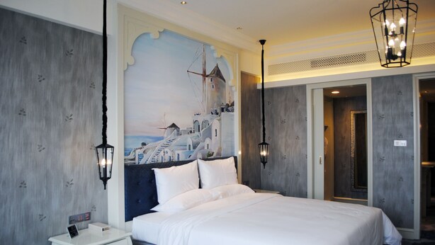 A hotel room with a large bed, a nightstand, a wall-mounted clock, and a door leading to another room. - Huaqing Aegean Inter Hot Spring Resort (Xi'an)