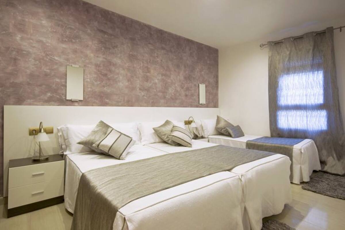 A hotel room with two beds, a nightstand, a lamp, and a window with curtains.
