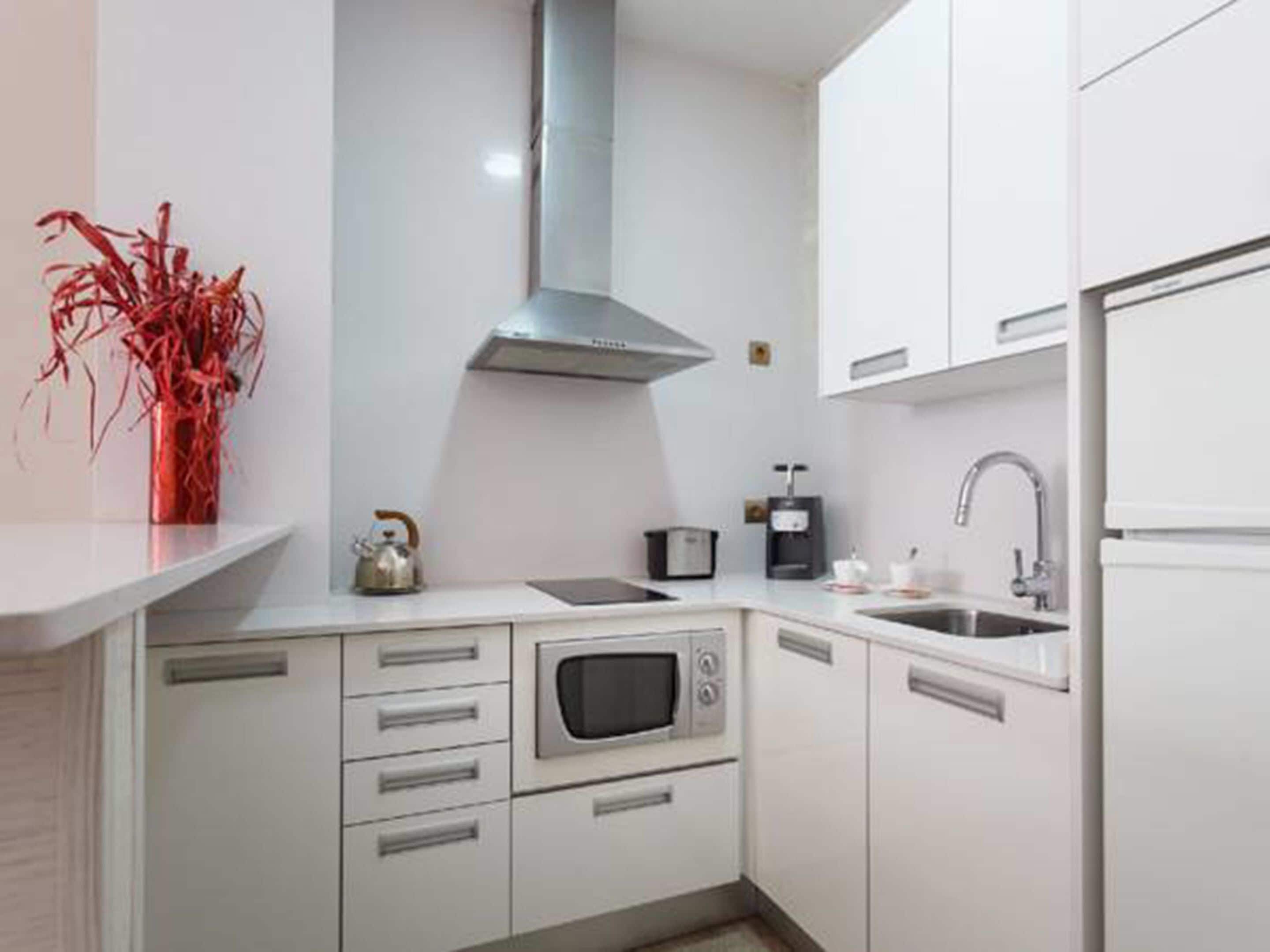 Una cocina moderna con armarios blancos, una campana extractora de acero inoxidable, un horno empotrado, una cafetera y un lavabo.