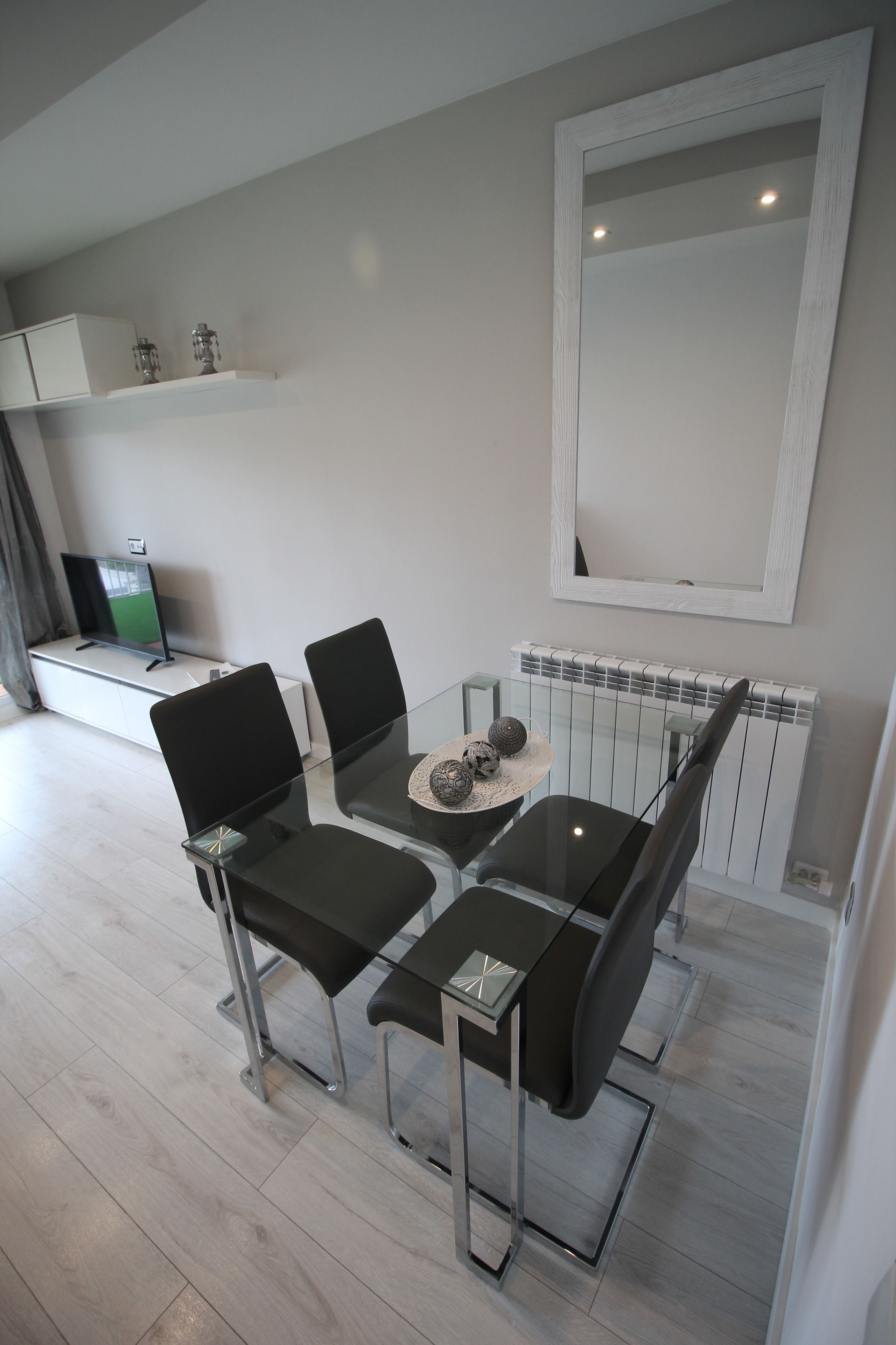 Et moderne spiseområde med et glasbord, sorte stole og en dekorativ midtpunkt.