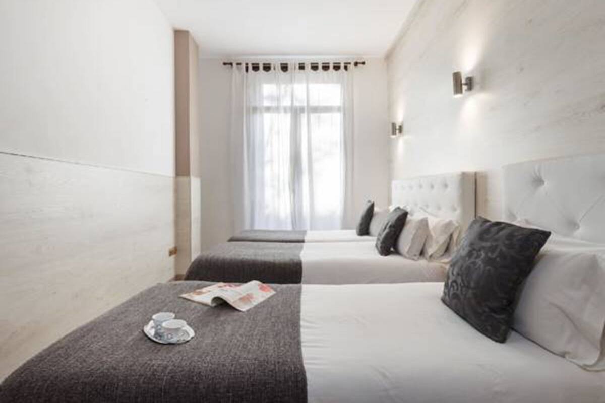 A hotel room with a large bed, a smaller bed, and a bench with a magazine and a cup.