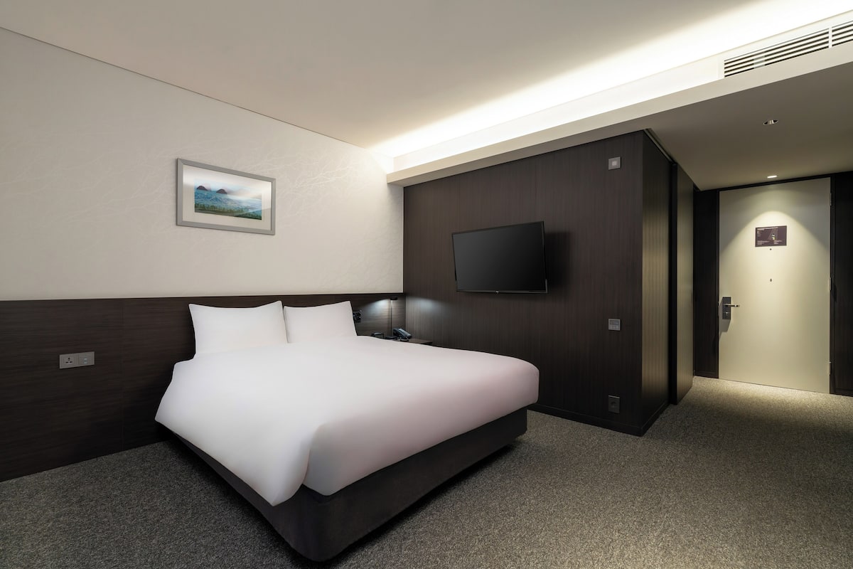 A modern hotel room with a large bed, a flat-screen TV mounted on the wall, and a small painting on the wall.
