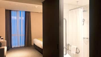 Habitación de hotel con cama, baño con ducha y vistas al exterior por una ventana.