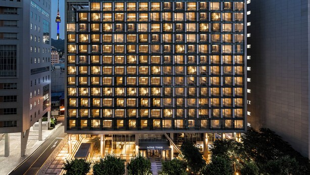 Un hotel moderno con una cuadrícula de ventanas iluminadas, un cartel llamativo en la parte superior y vistas del área urbana circundante.