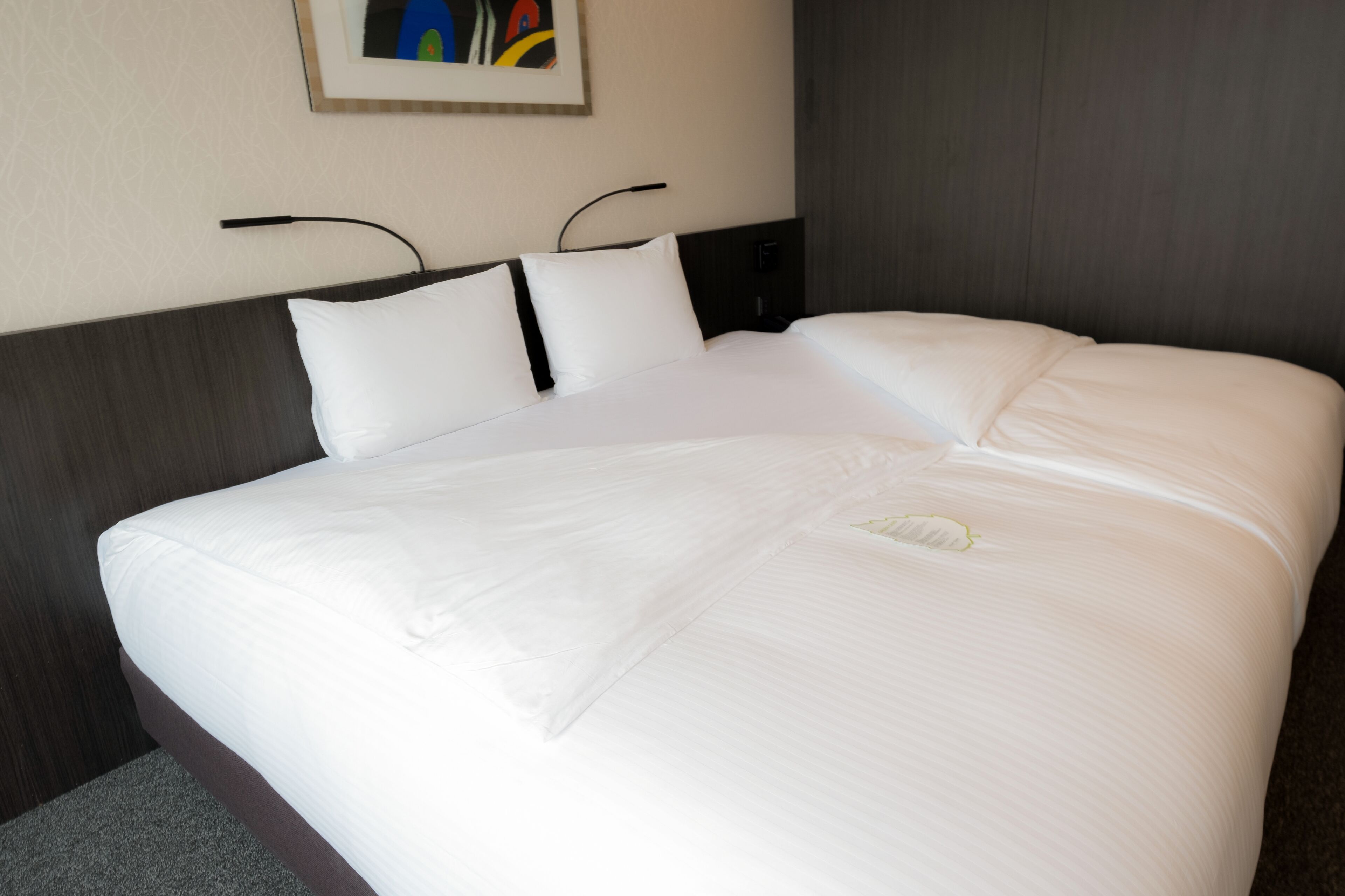 A large bed with white linens, a dark headboard, and a painting on the wall.