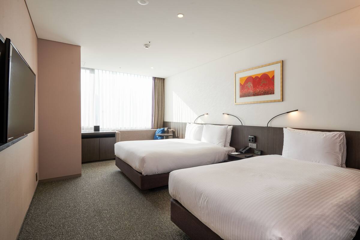 A hotel room with two beds, a TV, a desk, and a window with curtains.