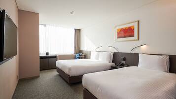A hotel room with two beds, a TV, a desk, and a window with curtains.