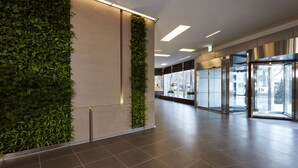 Un vestíbulo moderno con un jardín vertical verde, ventanas amplias y un piso de baldosas limpias.