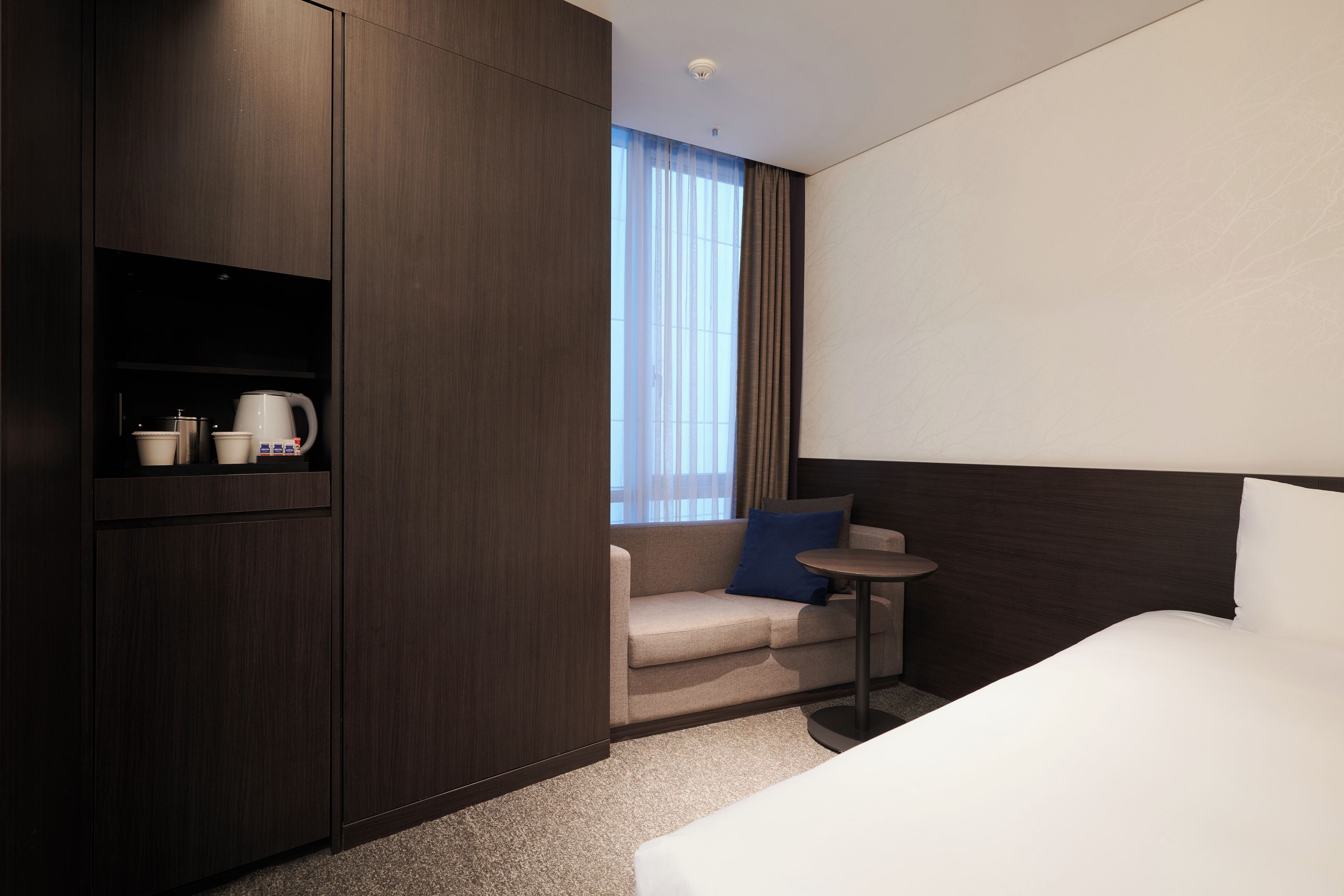 A hotel room with a bed, a sofa, a small table, and a cabinet with a coffee maker.