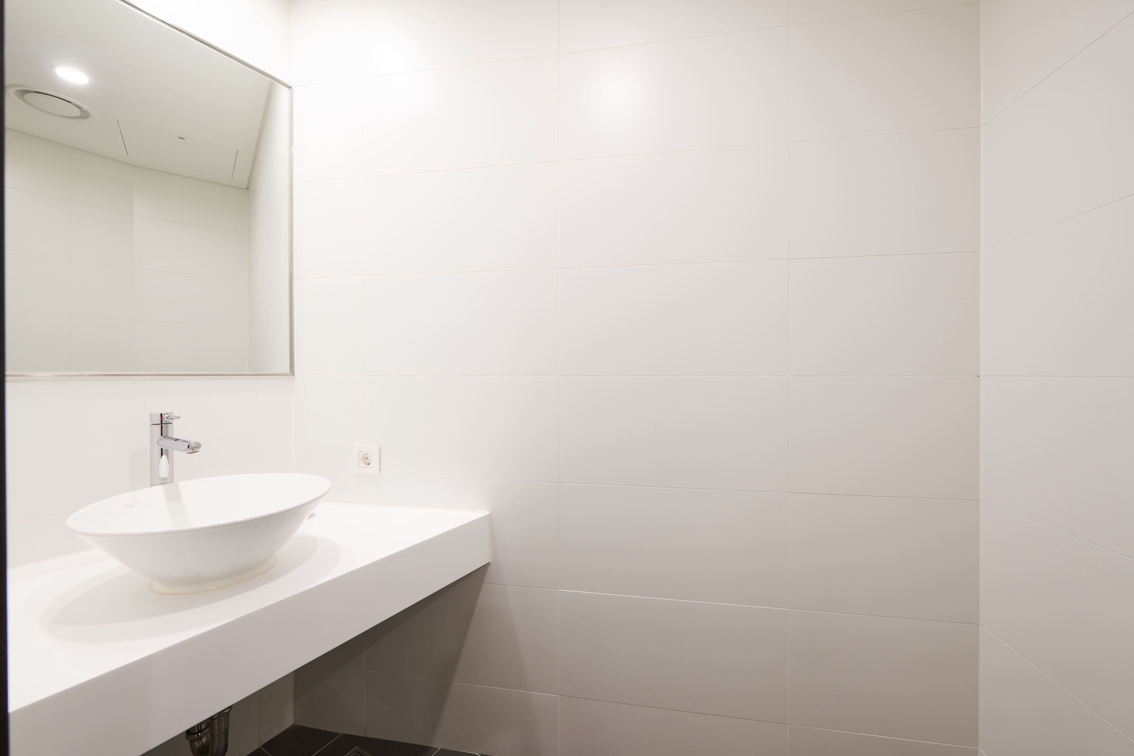 Un baño moderno con lavamanos blanco, un espejo y azulejos blancos.