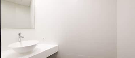 Un baño moderno con lavamanos blanco, un espejo y azulejos blancos.