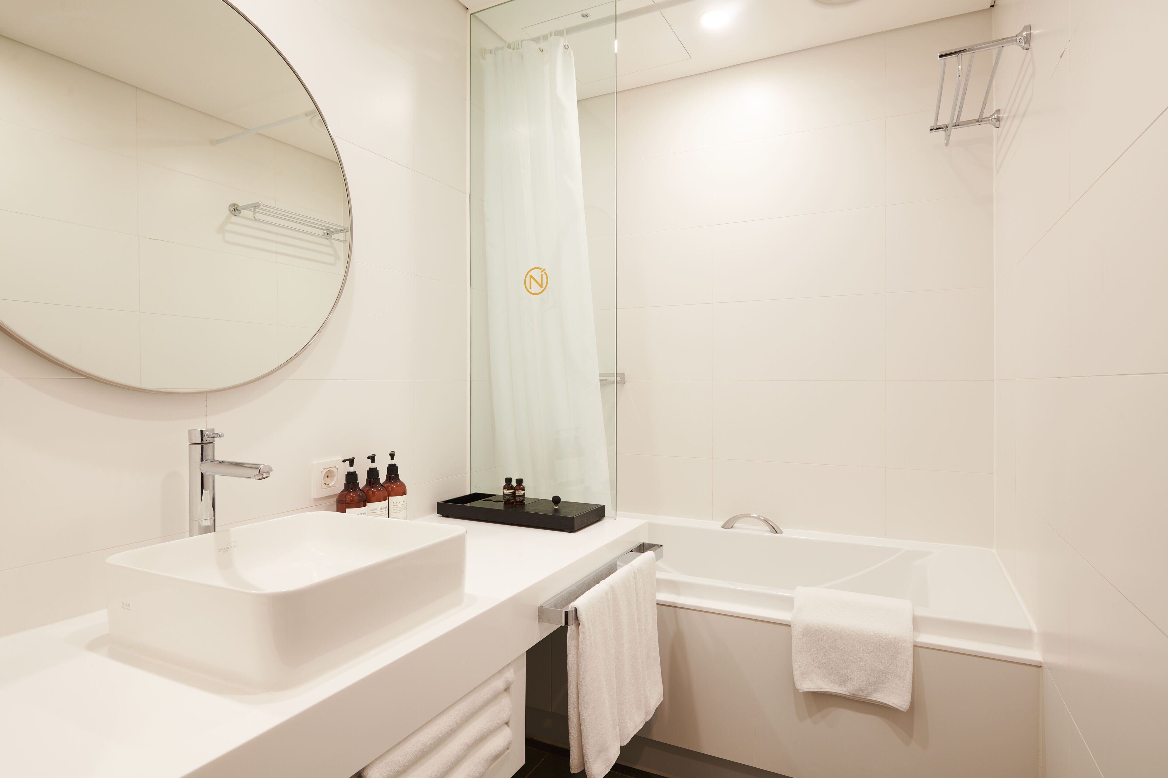 A modern bathroom with a large mirror, a white sink, a bathtub, and a shower curtain.