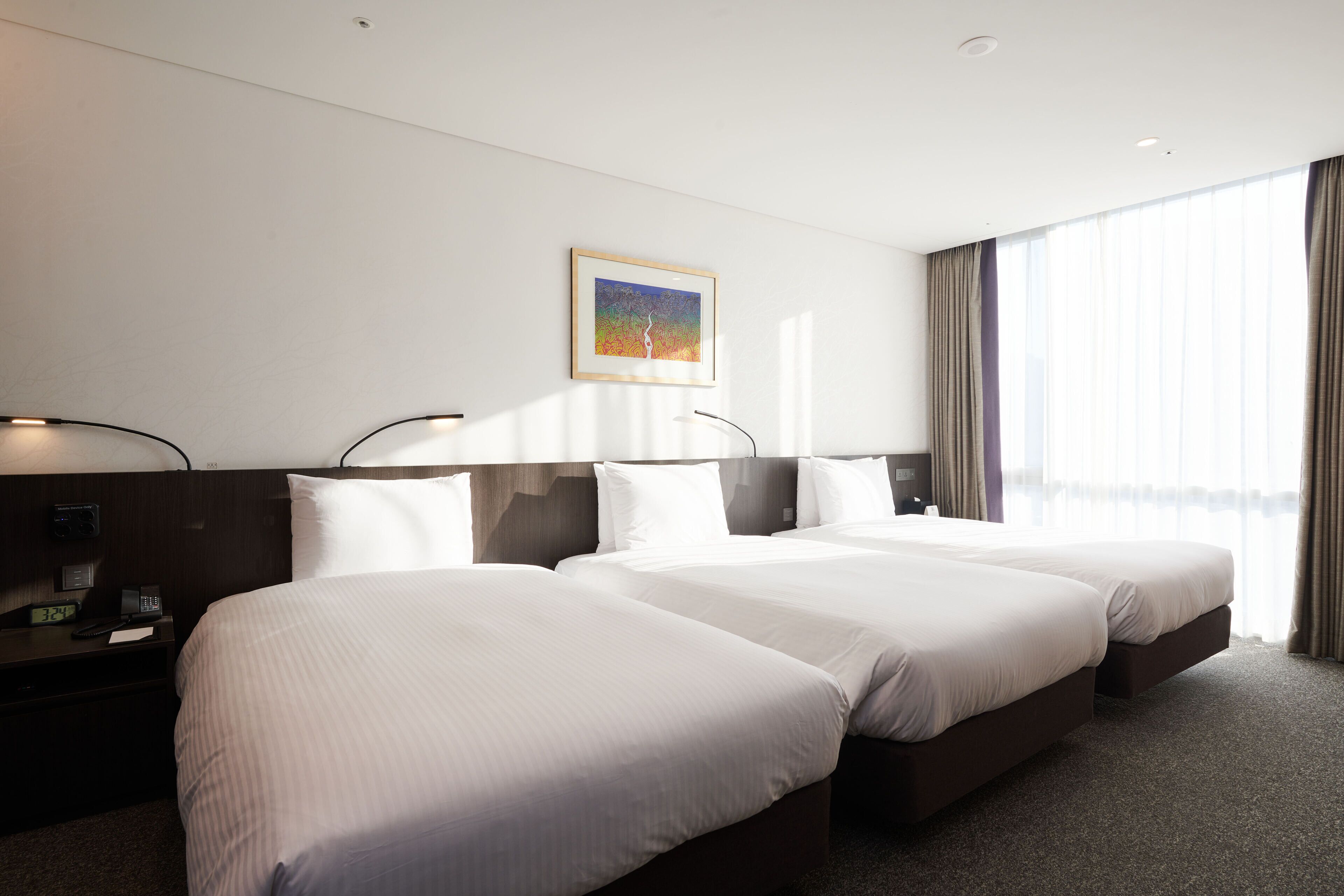 A hotel room with two beds, a painting on the wall, a nightstand with a phone, and a window with curtains.