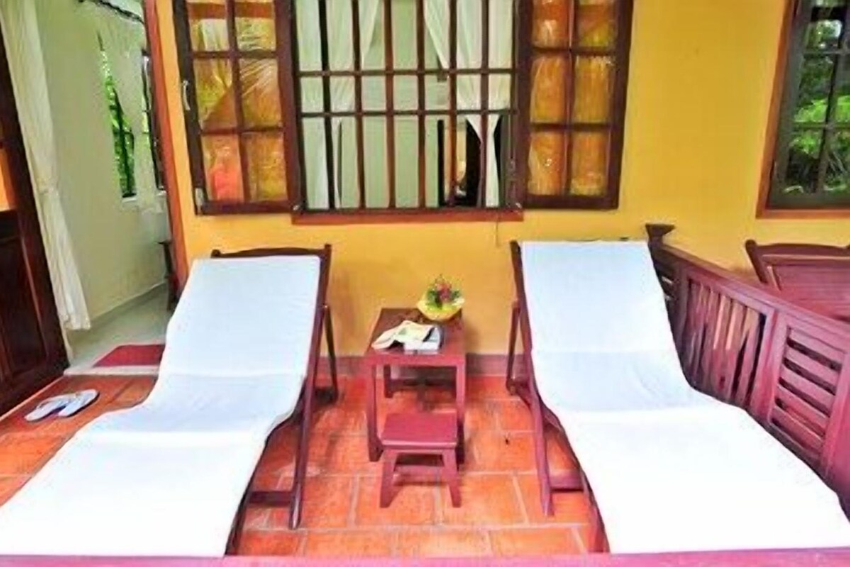 A room with two single beds, a small table with a plant, and a window with bars.