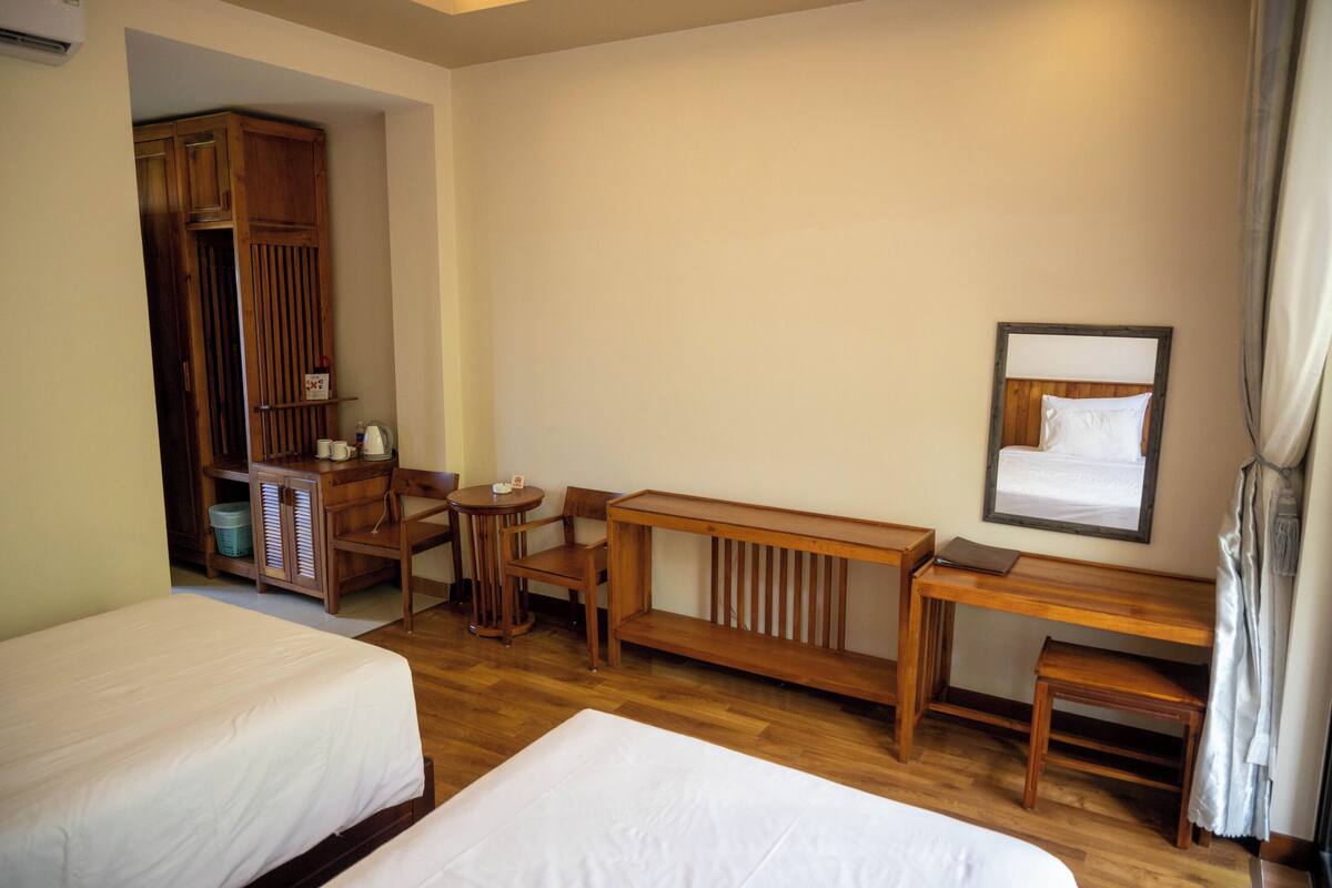 Une chambre d’hôtel avec deux lits, un bureau en bois, une chaise, une petite table et une armoire.