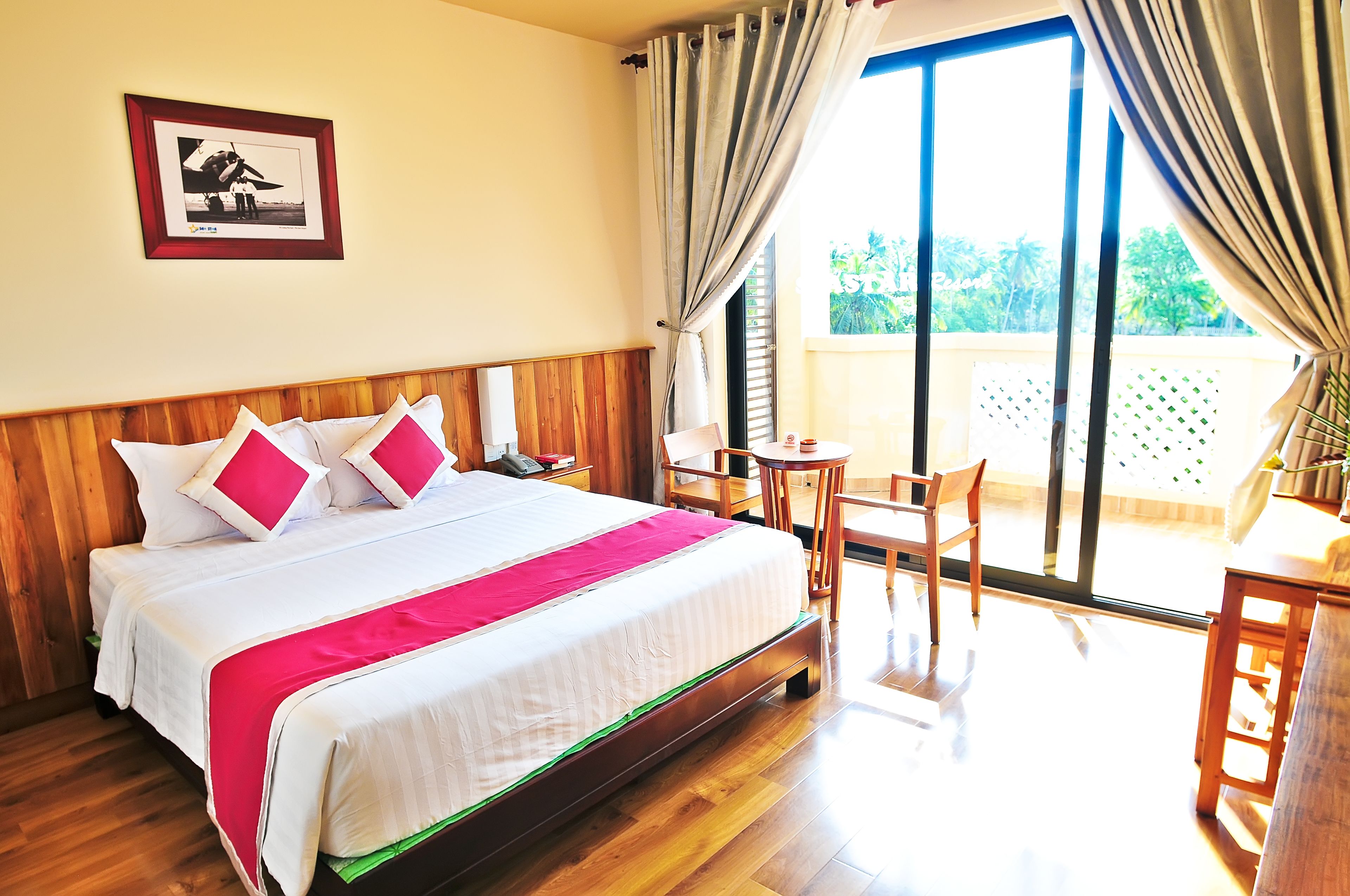 A hotel room with a bed, a desk, a chair, and a balcony with a view of greenery.