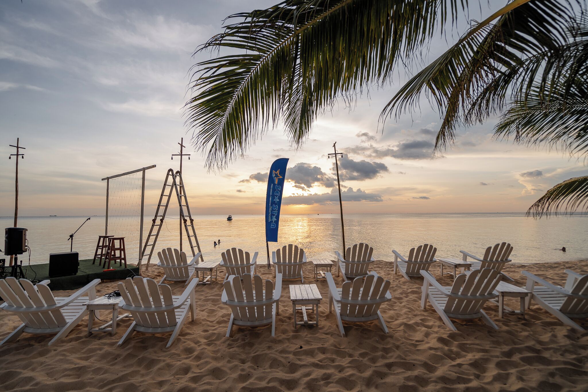 Uma praia com cadeiras brancas e um palco com equipamento musical.