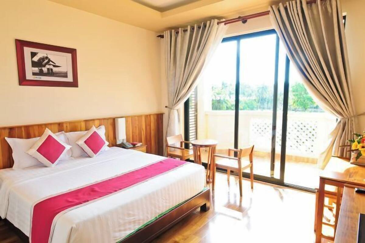 Une chambre d’hôtel avec un lit, un bureau, une chaise et un balcon avec des rideaux.