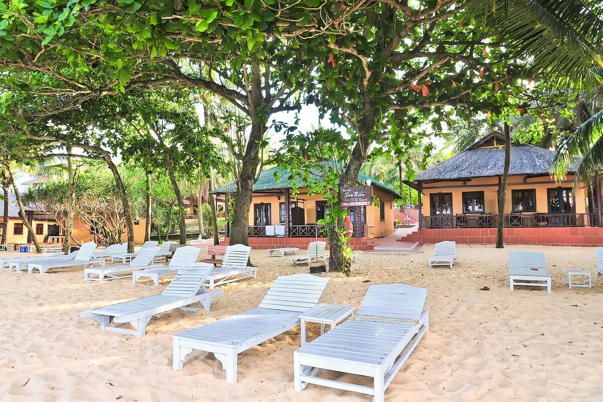 Une plage avec des chaises longues blanches et un bâtiment doté d’un toit de chaume.