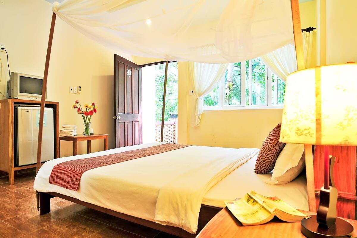 Une chambre à coucher bien rangée, avec un lit, une lampe de chevet et un téléviseur posé sur une commode en bois.