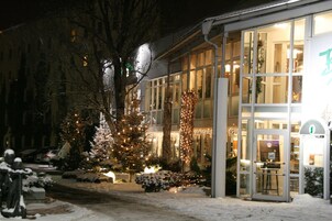 Un edificio con fachada de vidrio, suelo cubierto de nieve y luces navideñas.
