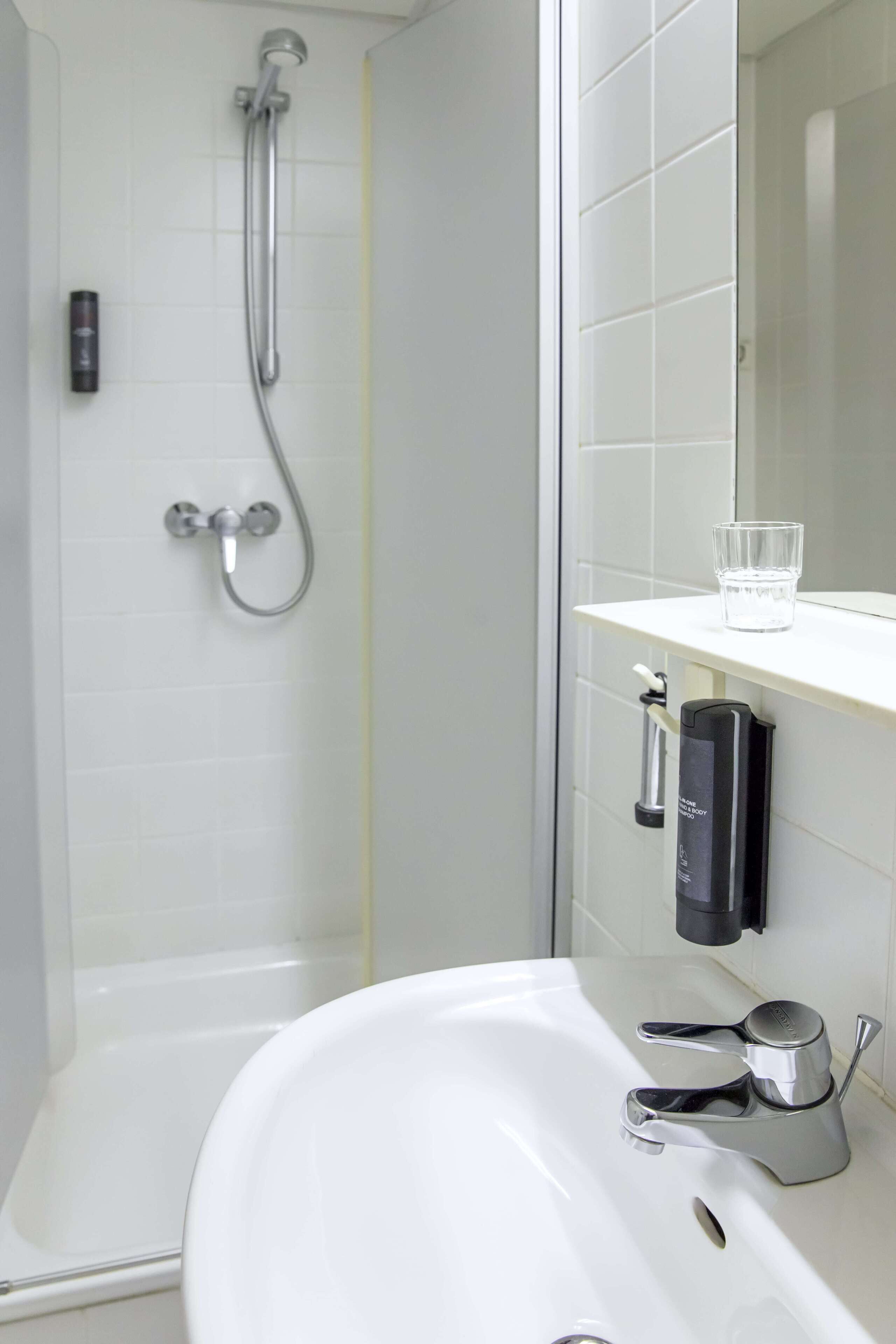 Un baño con un lavabo blanco, un cabezal de ducha de mano y un vaso de agua sobre el mostrador.