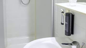 Un baño con un lavabo blanco, un cabezal de ducha de mano y un vaso de agua sobre el mostrador.