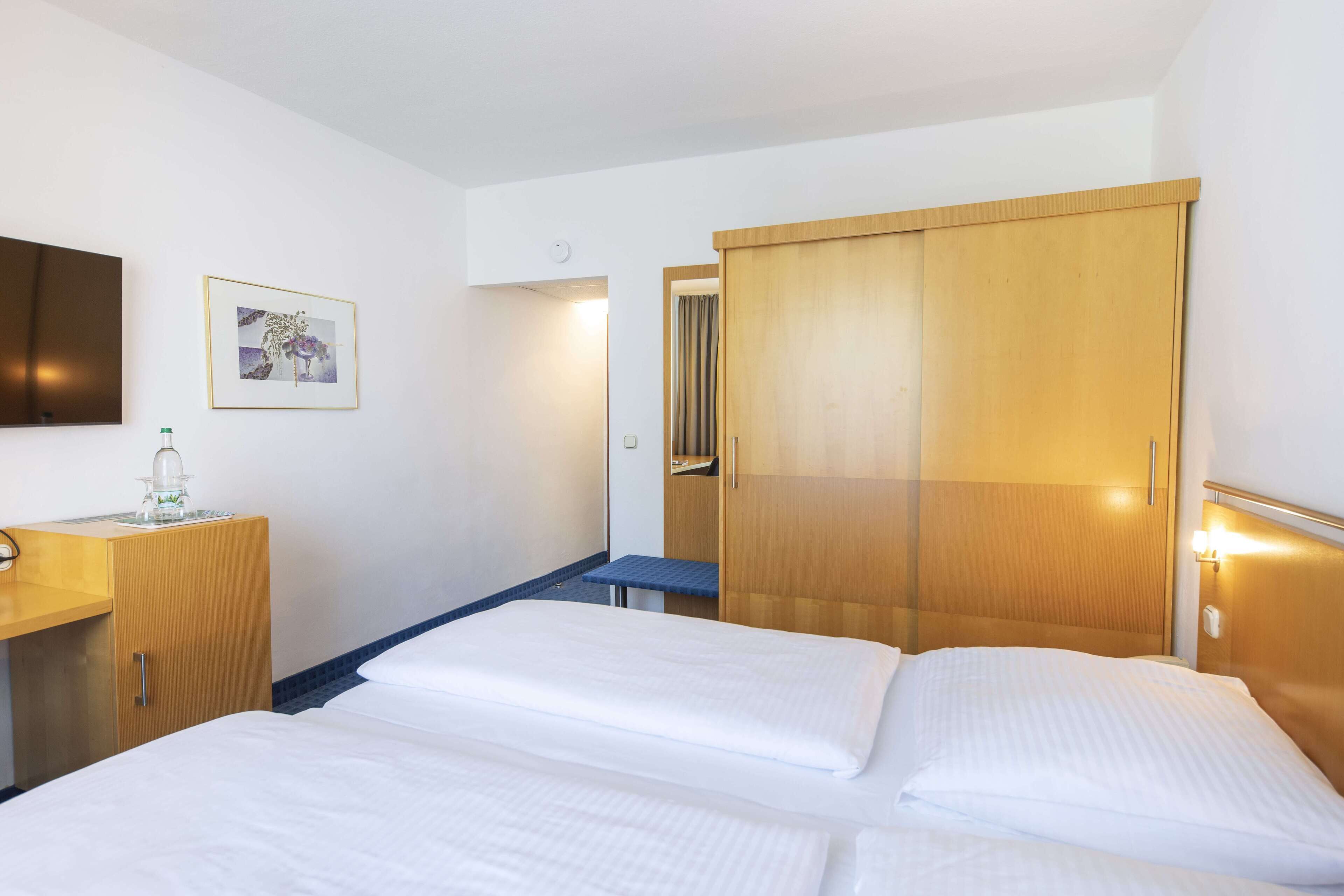 A hotel room with a bed, a desk, a wardrobe, and a mirror.