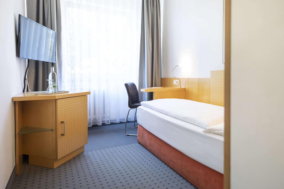 A hotel room with a bed, a desk with a chair, a TV, and a minibar.
