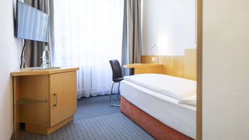 Ett hotellrum med en säng, ett skrivbord med en stol, en TV och en minibar.