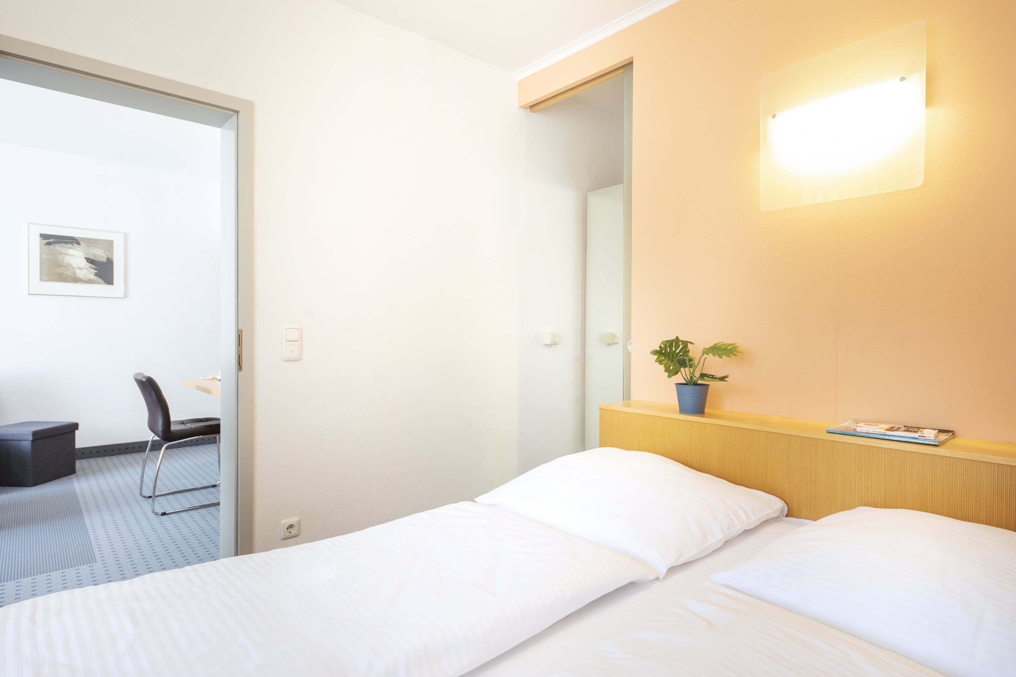 A hotel room with a single bed, a chair, a small table, and a potted plant.