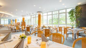 Un comedor amplio con mesas redondas, sillas de madera y ventanas grandes que ofrecen vistas al verdor.